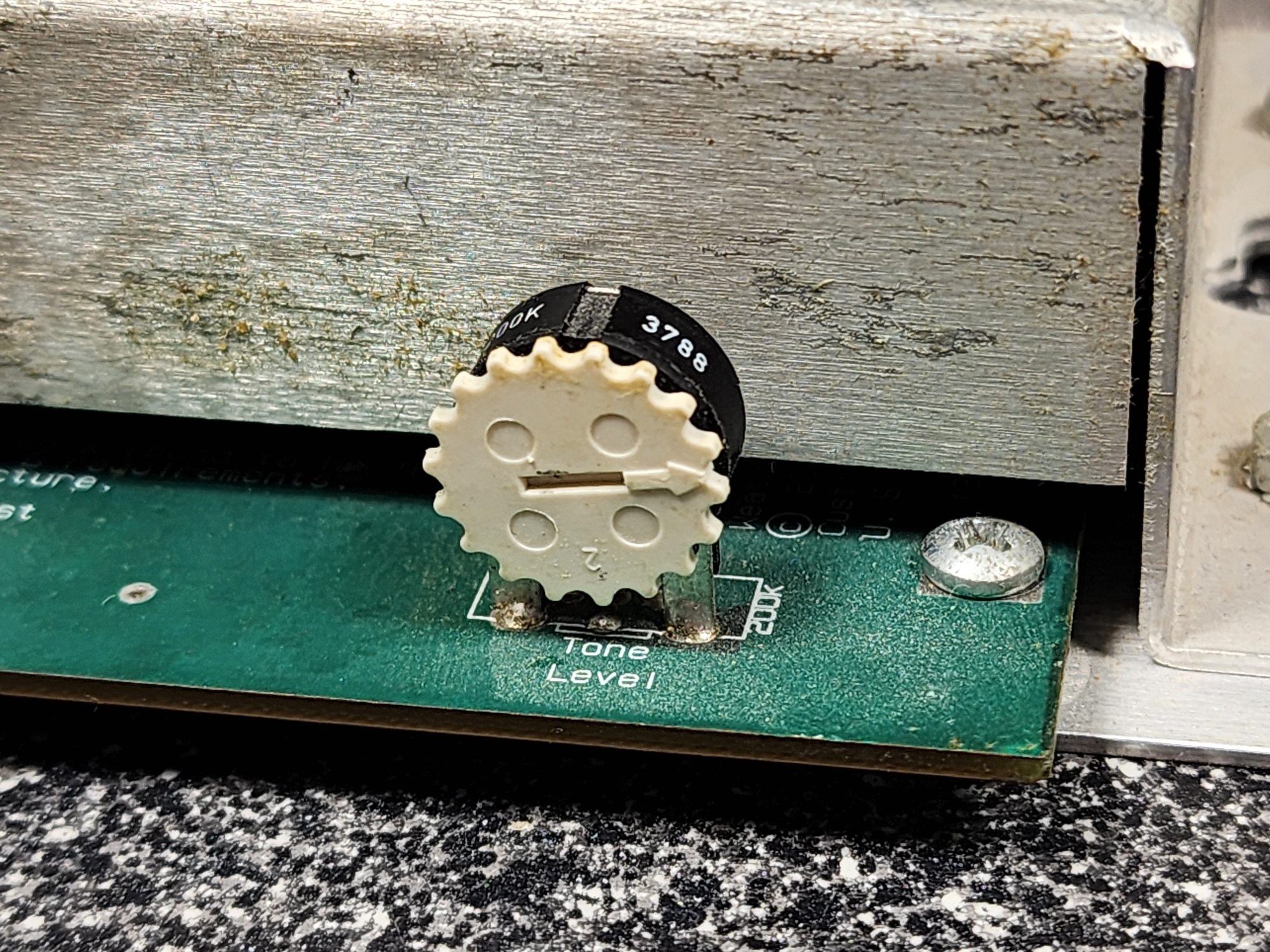 Picture 6: A detailed photograph of the potentiometer. There is a plastic gear-shaped wheel with a horizontal slot for a screwdriver, with an arrow pointing in line with the hole. The circuit board has a label for the position of this component, reading: 'Tone Level'.