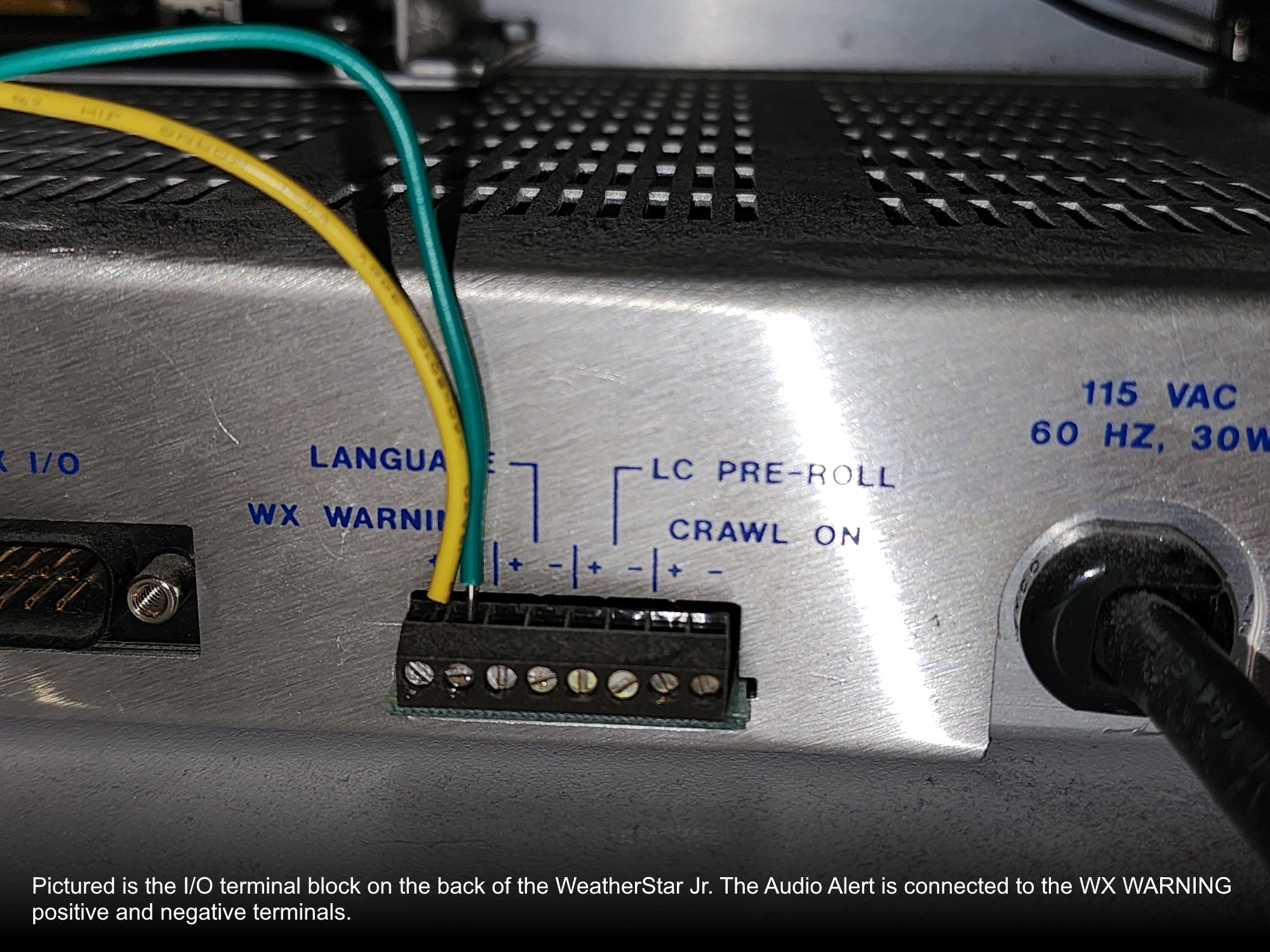 Picture 7: A close-up, rear view of the Weather Star Jr's I/O terminal block as it is wired to the Audio Alert. The terminal block has positive and negative terminals for the following four labels: 'WX WARNING,' 'LANGUAGE,' 'LC PRE-ROLL,' and 'CRAWL ON.' A yellow wire is placed into the positive terminal of the WX WARNING block, and a green wire is placed into the negative terminal.