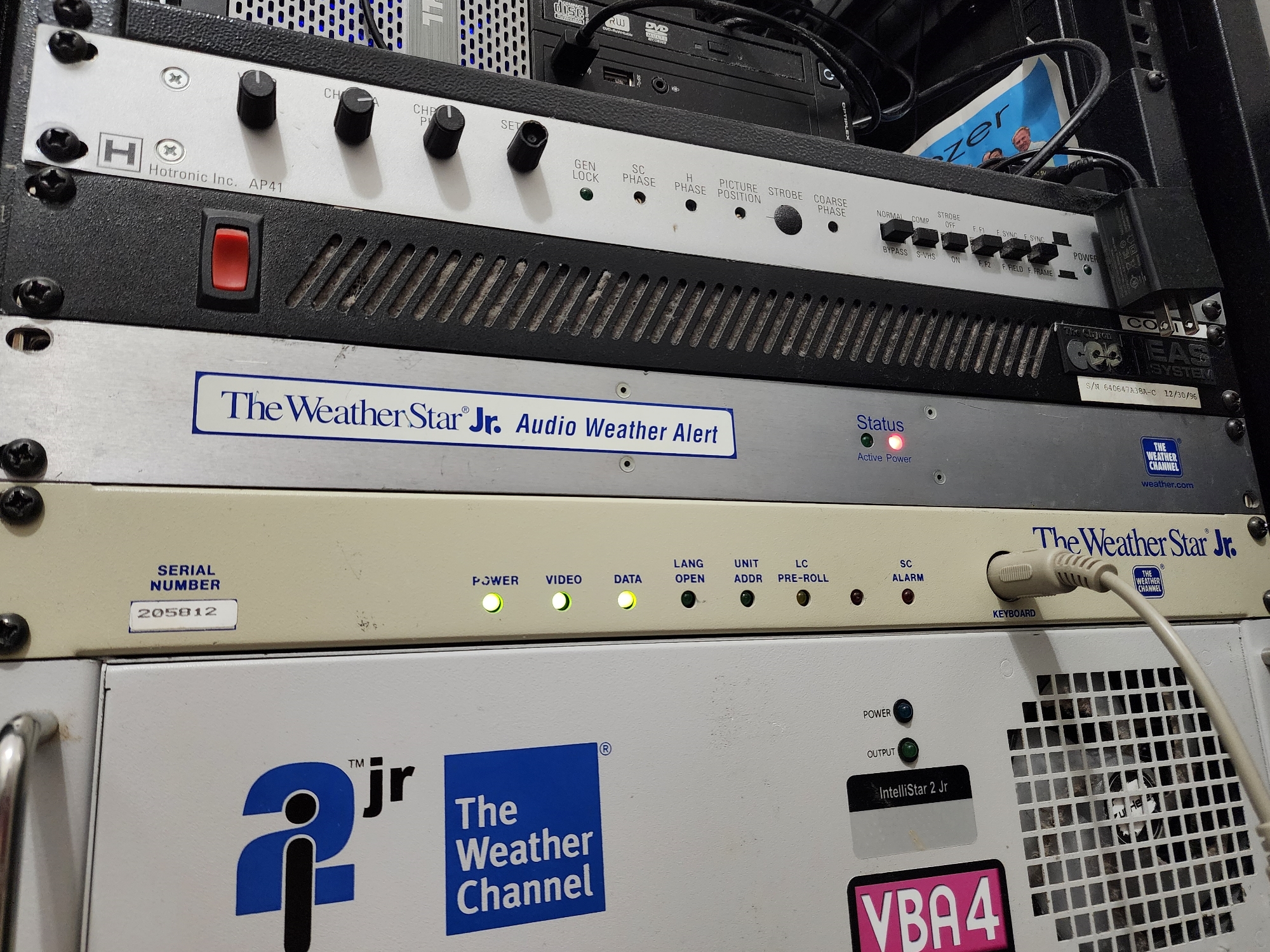 Picture 8: The Weather Star Jr Audio Weather Alert is placed inside of a rack on top of The Weather Star Jr. The red power LED is lit up.